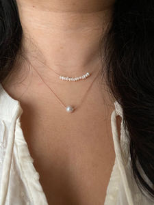 white freshwater pearl bar on a silk cord, shown worn along with a single pearl necklace. 