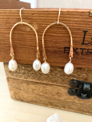 white freshwater pearl drops suspended from a gold fill upside down U shaped frame displayed against a brown box 