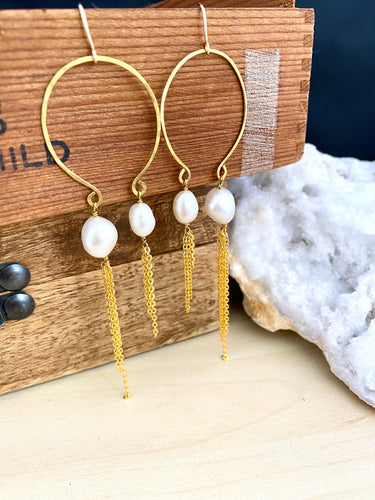 View of handmade gold and freshwater pearl boho statement earrings shown hung from a brown box.  Image shows the approximate length of the earrings and the length of the asymmetrical chain tassels 