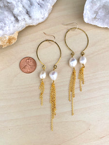 Image of asymmetrical freshwater pearl and gold tassel earrings suspended from an inverted hammered brass hoop and attached to 14kgold fill ear wires. Earring are on a table with a penny next to the earrings to show scale and size