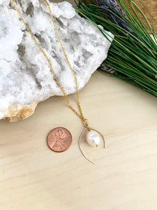 wish bone shaped gold metal frame with a freshwater pearl enclosed within in pendant frame.  